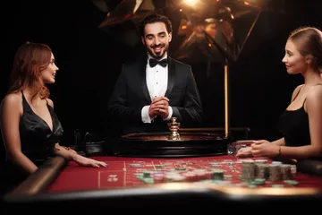A professional dealer in a tuxedo greeting players at the roulette table, symbolizing the authentic live casino feel at WAGIPLUS.